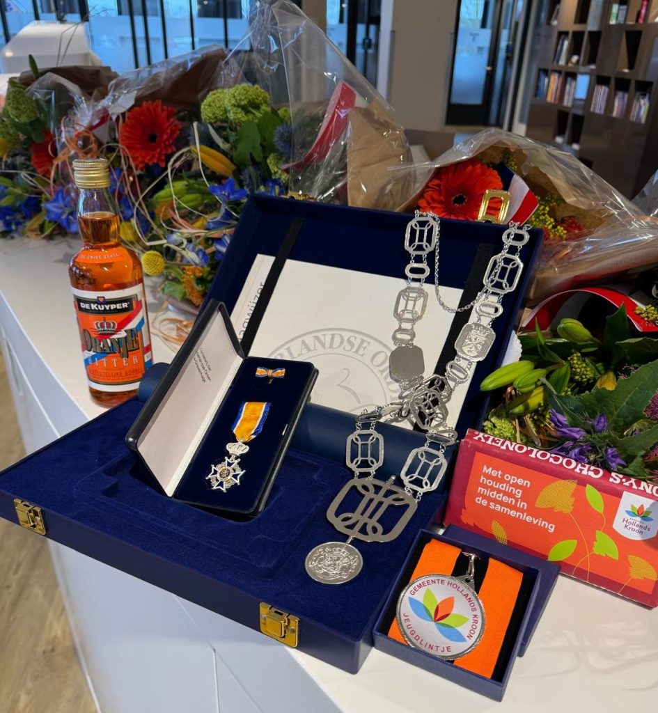 Koninklijke Onderscheiding, ambtsketting, jeugdlintje en bloemen op tafel.